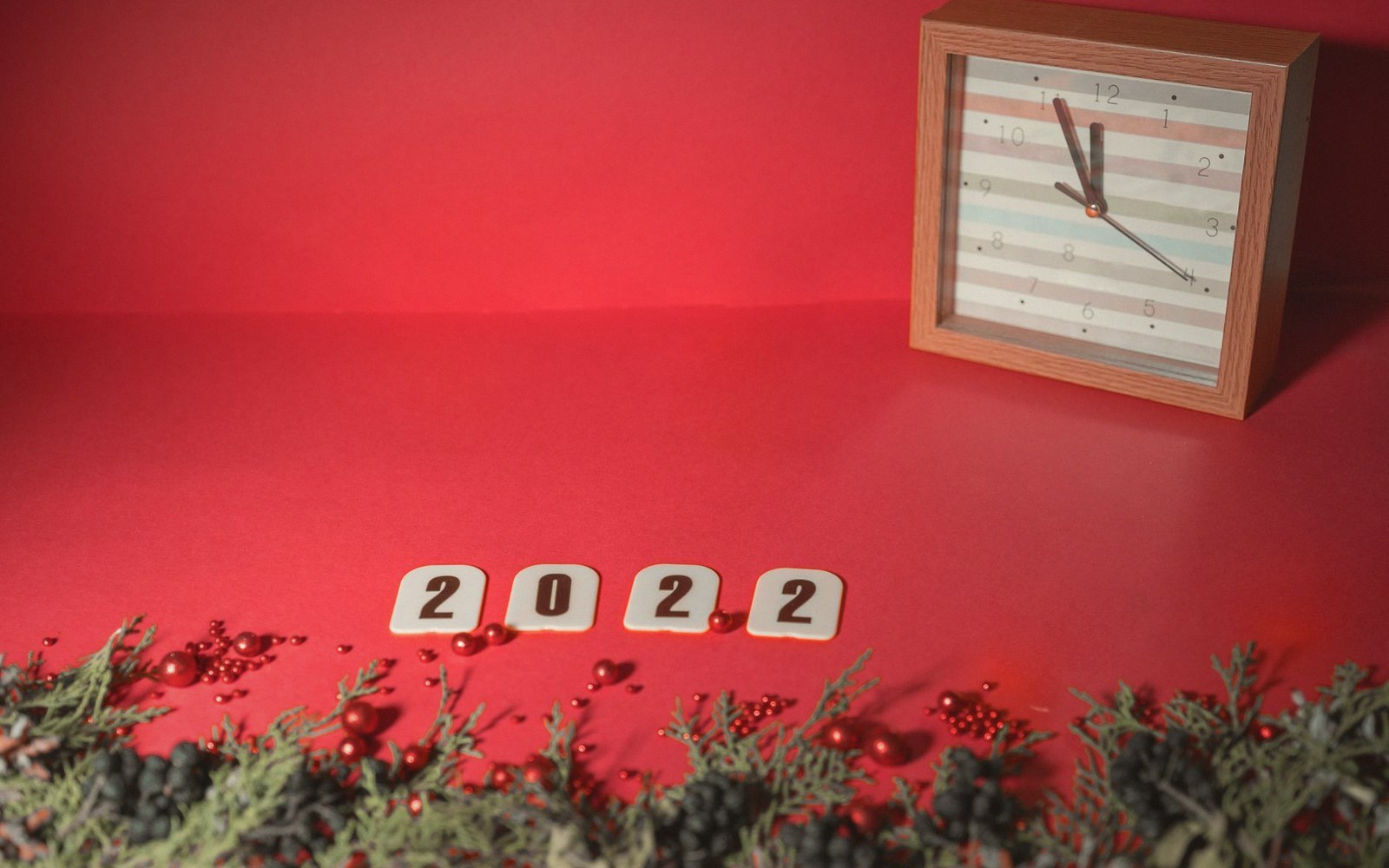 Square wooden clock and tile numbers spelling 2022 on a red background with pine sprigs