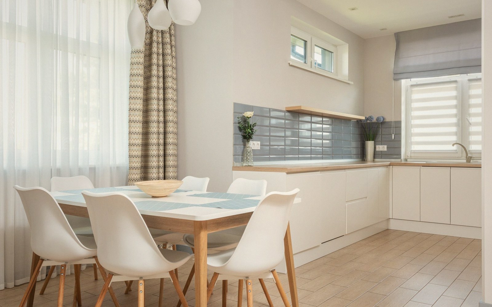 Dining table with white chairs beside a white kitchen with gray tile backsplash