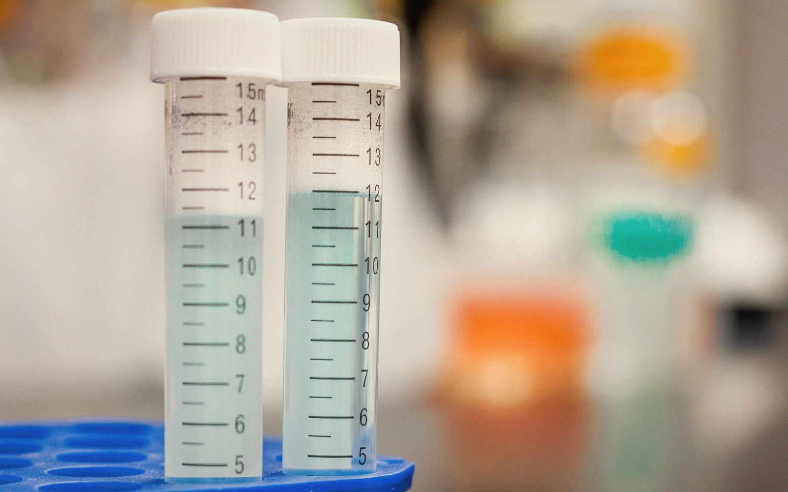 Two graduated lab vials with liquid samples sit in a blue rack