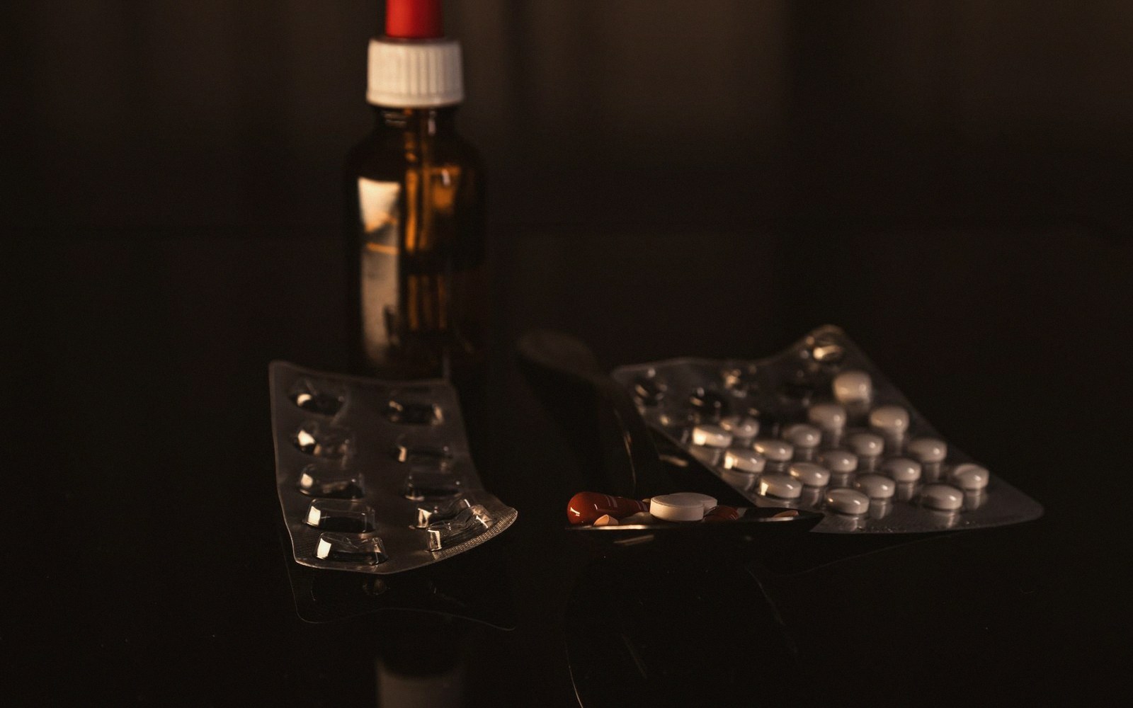 Pill blister packs and a brown medicine bottle on a dark reflective surface
