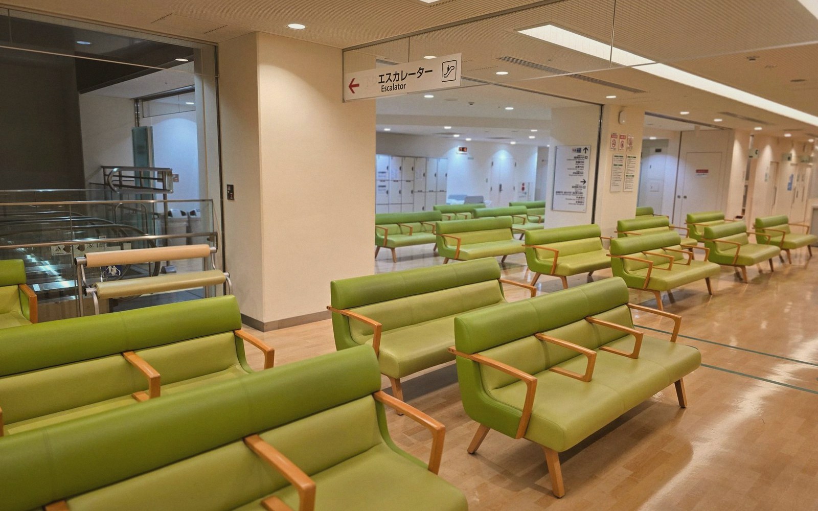 Rows of green benches fill a waiting area near an escalator sign in Japanese